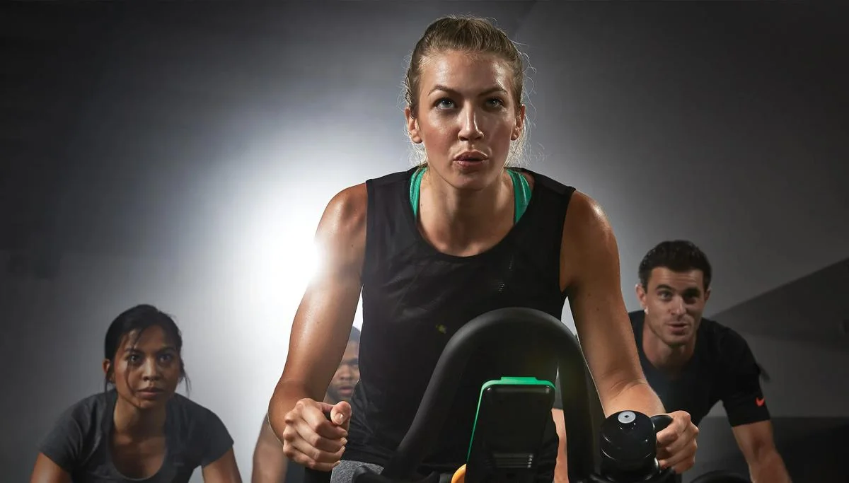 A person in a black workout tank facing forward during a group cycling class.